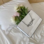 White and pink peonies elegantly placed in a Chanel bag on a white pillow, depicting luxury and simplicity.